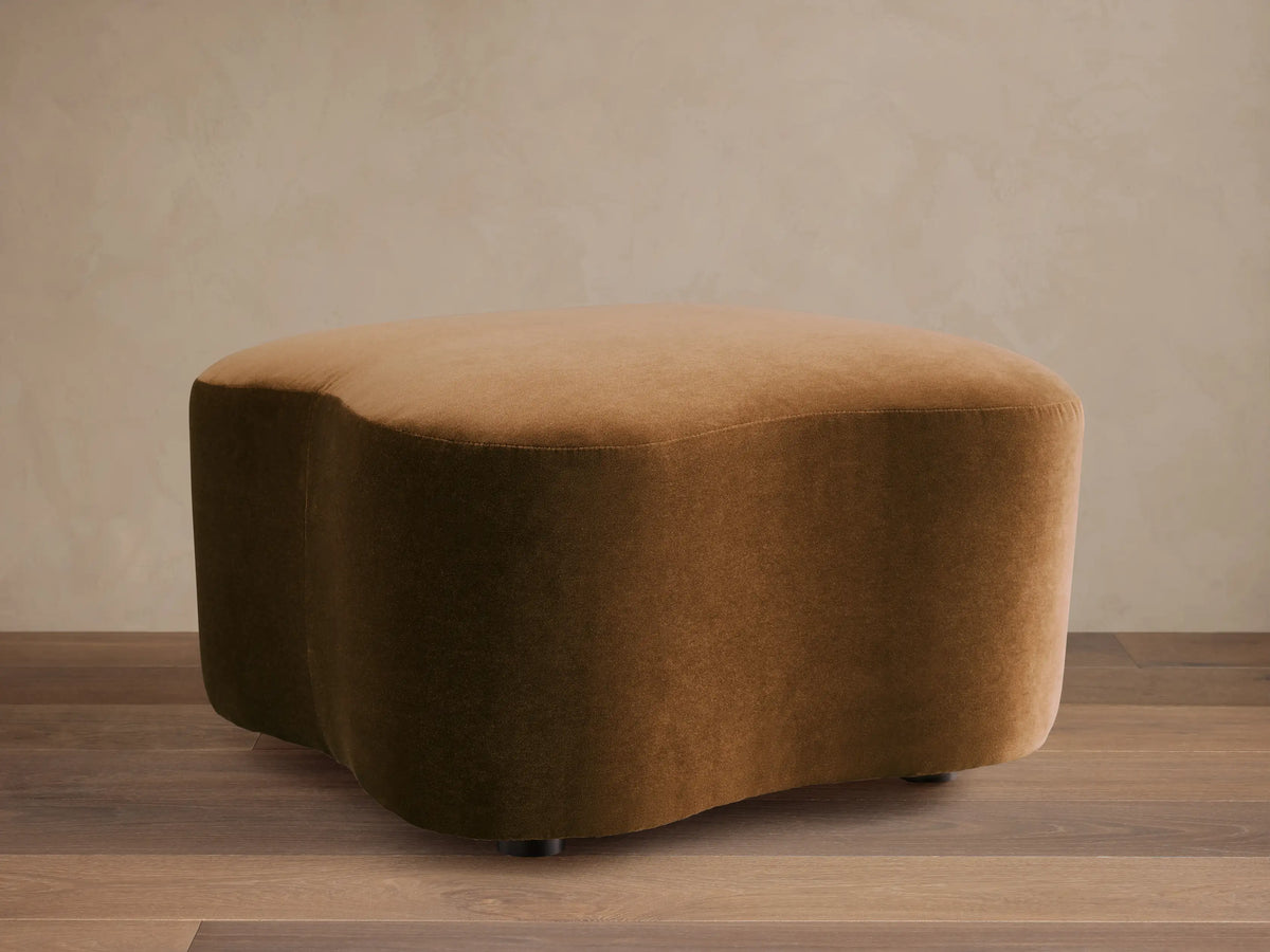 Front view of the cognac Barbey Ottoman, featuring an irregular organic shape and soft velvet upholstery.