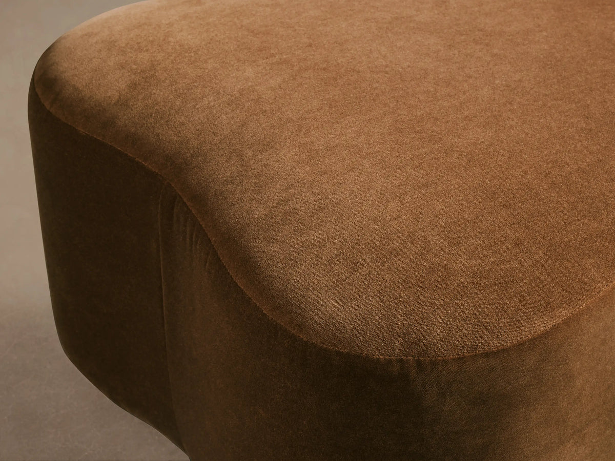 Close-up of the rich brown Barbey Ottoman, featuring its soft, textured upholstery and gently curved, rounded shape.