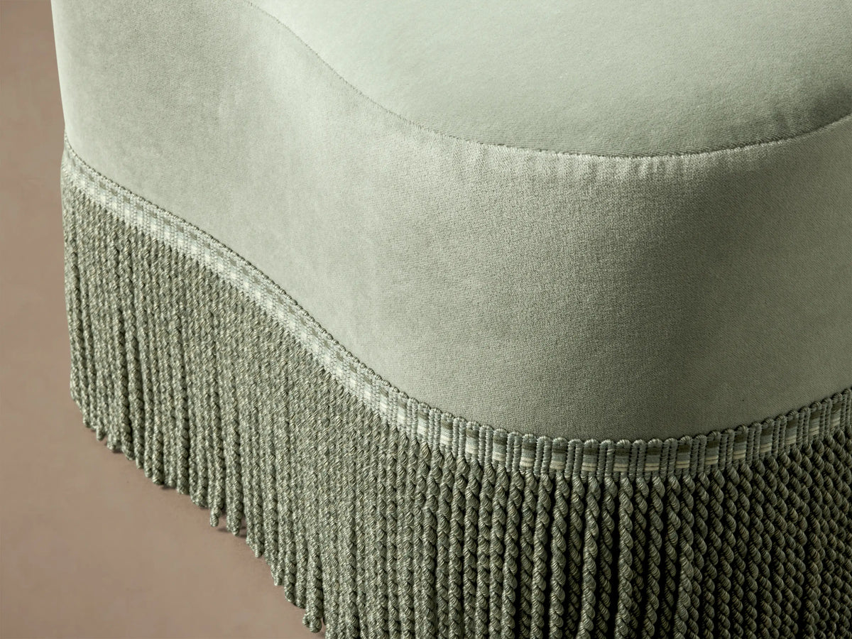 Close-up of the light green Barbey Ottoman with Fringe, highlighting the velvet-like fabric and intricate braided fringe detail.