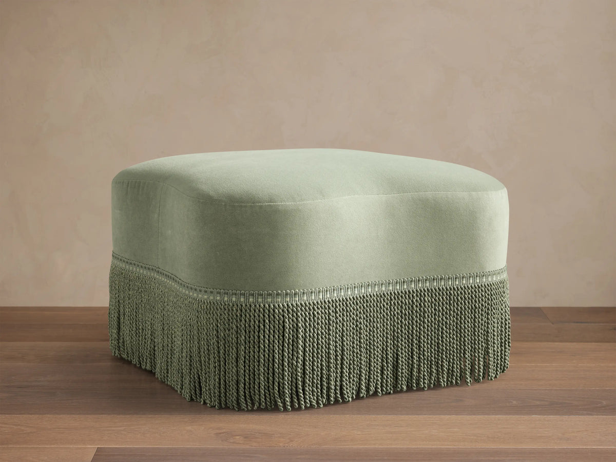 Front view of sage green Barbey Ottoman with Fringe, featuring dense, matching fringe along its lower edge.
