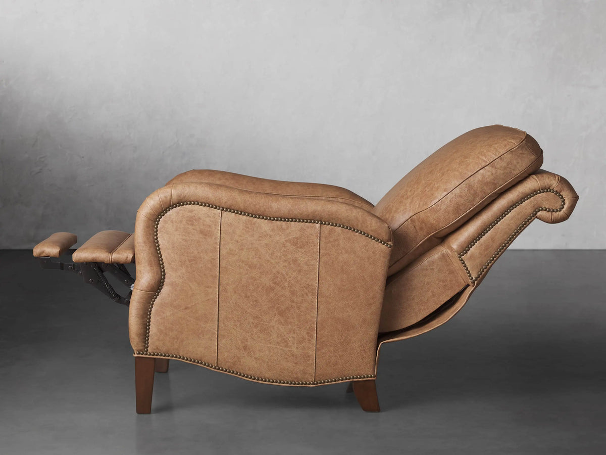 Angled side view of Brooklyn Leather Recliner. Light brown distressed leather, rolled arms, nailhead trim, wooden legs.