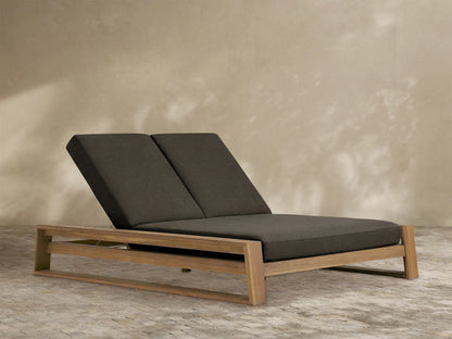 Canyon Outdoor Teak Double Chaise with a natural teak wood frame and two elevated charcoal cushions, viewed from an angle.