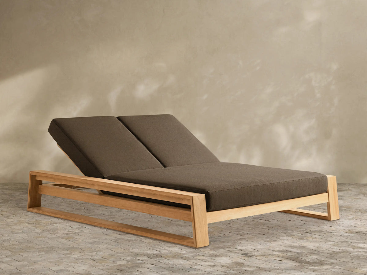 Canyon Outdoor Teak Double Chaise with light brown wooden frame & two dark brown cushions, backrests reclined, on white.
