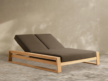 Canyon Outdoor Teak Double Chaise with light brown wooden frame & two dark brown cushions, backrests reclined, on white.