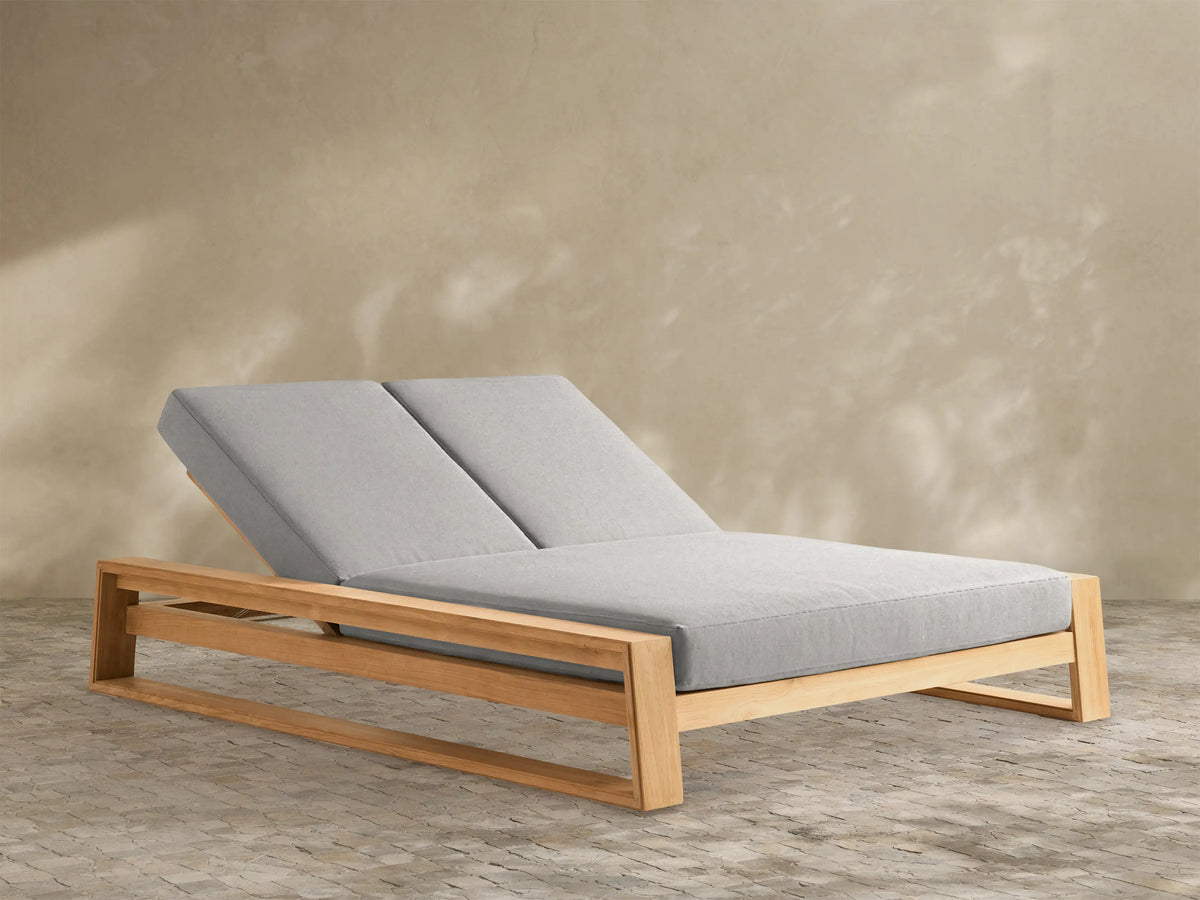 Canyon Outdoor Teak Double Chaise with light brown wooden frame and two light gray cushions, both backrests reclined, viewed at an angle.