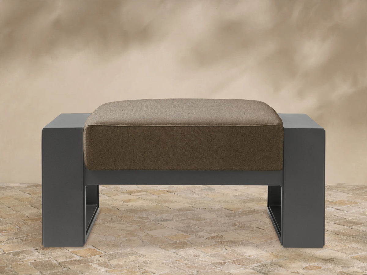 Canyon Outdoor Aluminum Ottoman: Dark gray aluminum frame, light brown cushion with rounded edges, front view on white background.