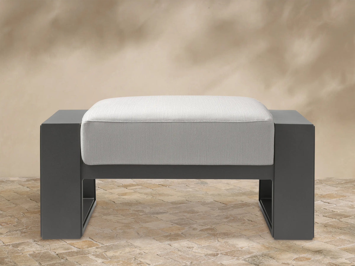 Canyon Outdoor Aluminum Ottoman, front view. Dark gray aluminum frame with a light gray cushioned top.