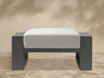 Canyon Outdoor Aluminum Ottoman, front view. Dark gray aluminum frame with a light gray cushioned top.