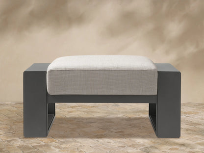Canyon Outdoor Aluminum Ottoman with dark gray aluminum frame and light beige textured cushion, front view on white.