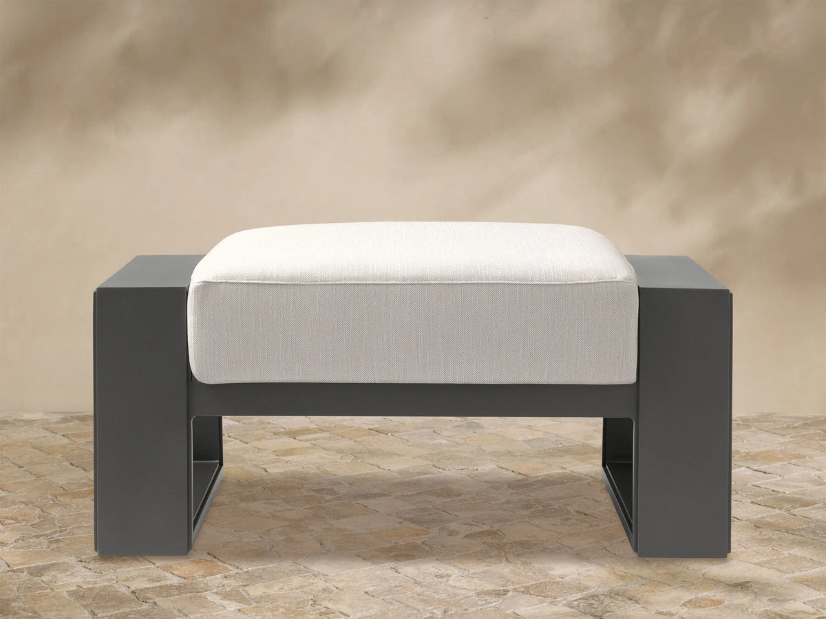 Canyon Outdoor Aluminum Ottoman with a matte dark gray rectangular frame and a light cream upholstered cushion, seen from the front.