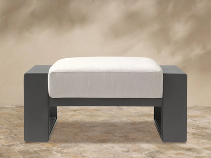 Canyon Outdoor Aluminum Ottoman with a matte dark gray rectangular frame and a light cream upholstered cushion, seen from the front.