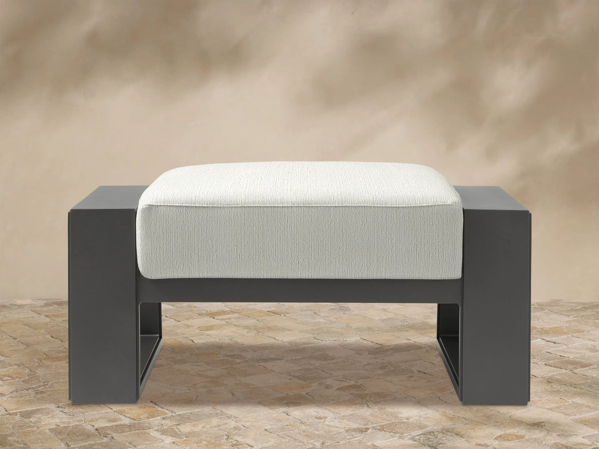 Canyon Outdoor Aluminum Ottoman with a dark gray frame and a light beige, textured fabric cushion, front view.