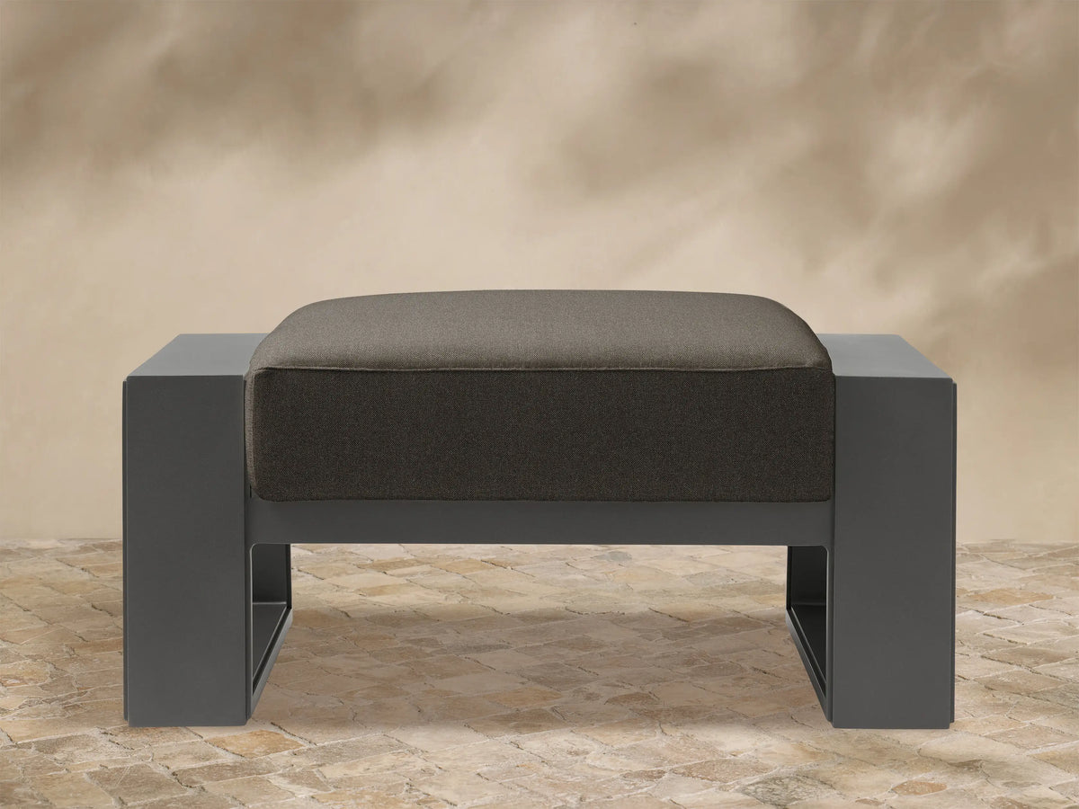 Front view of Canyon Outdoor Aluminum Ottoman. Dark charcoal aluminum frame supports a thick, textured gray-brown cushion.