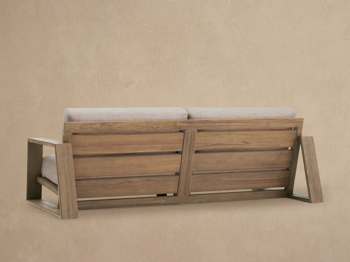 Front view of the Canyon Outdoor Teak Sofa with natural teak frame and light beige cushions on a paved patio.