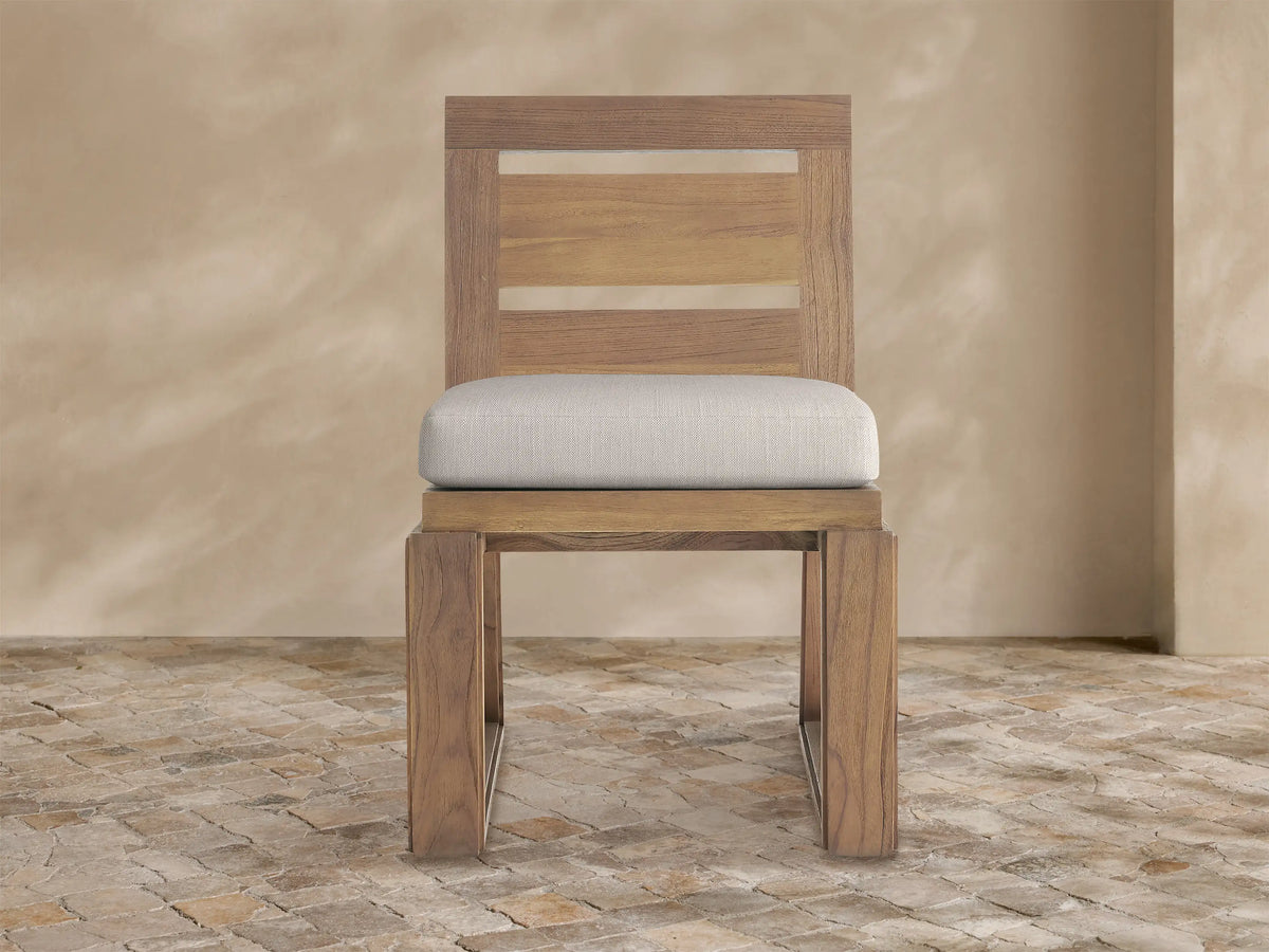 Canyon Outdoor Teak Dining Side Chair. Front view of a natural teak wood chair with slatted back and light beige cushion.