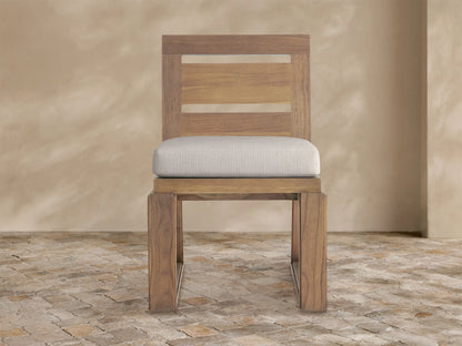 Canyon Outdoor Teak Dining Side Chair. Front view of a natural teak wood chair with slatted back and light beige cushion.