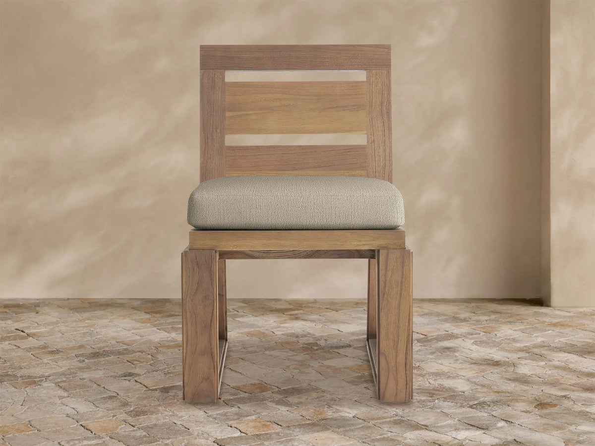 Canyon Outdoor Teak Dining Side Chair, front view. Natural teak wood frame with open slatted back and a light beige seat cushion.