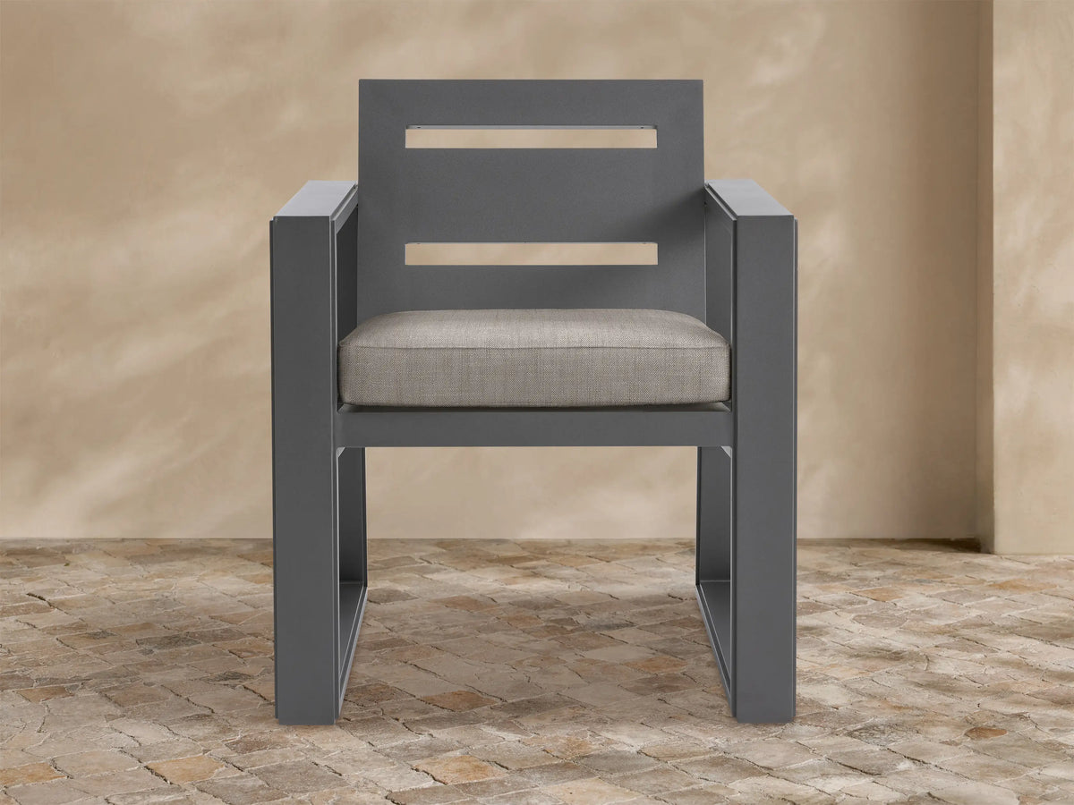 Front view of Canyon Outdoor Aluminum Dining Arm Chair, dark gray frame with two horizontal cutouts on back, light beige cushion.