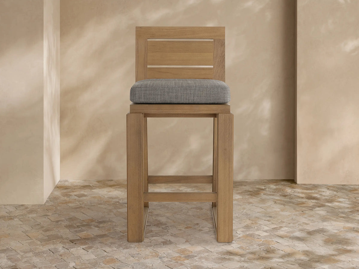 Front view of a light brown teak Canyon Outdoor Barstool with a slatted backrest and a dark grey fabric cushion.