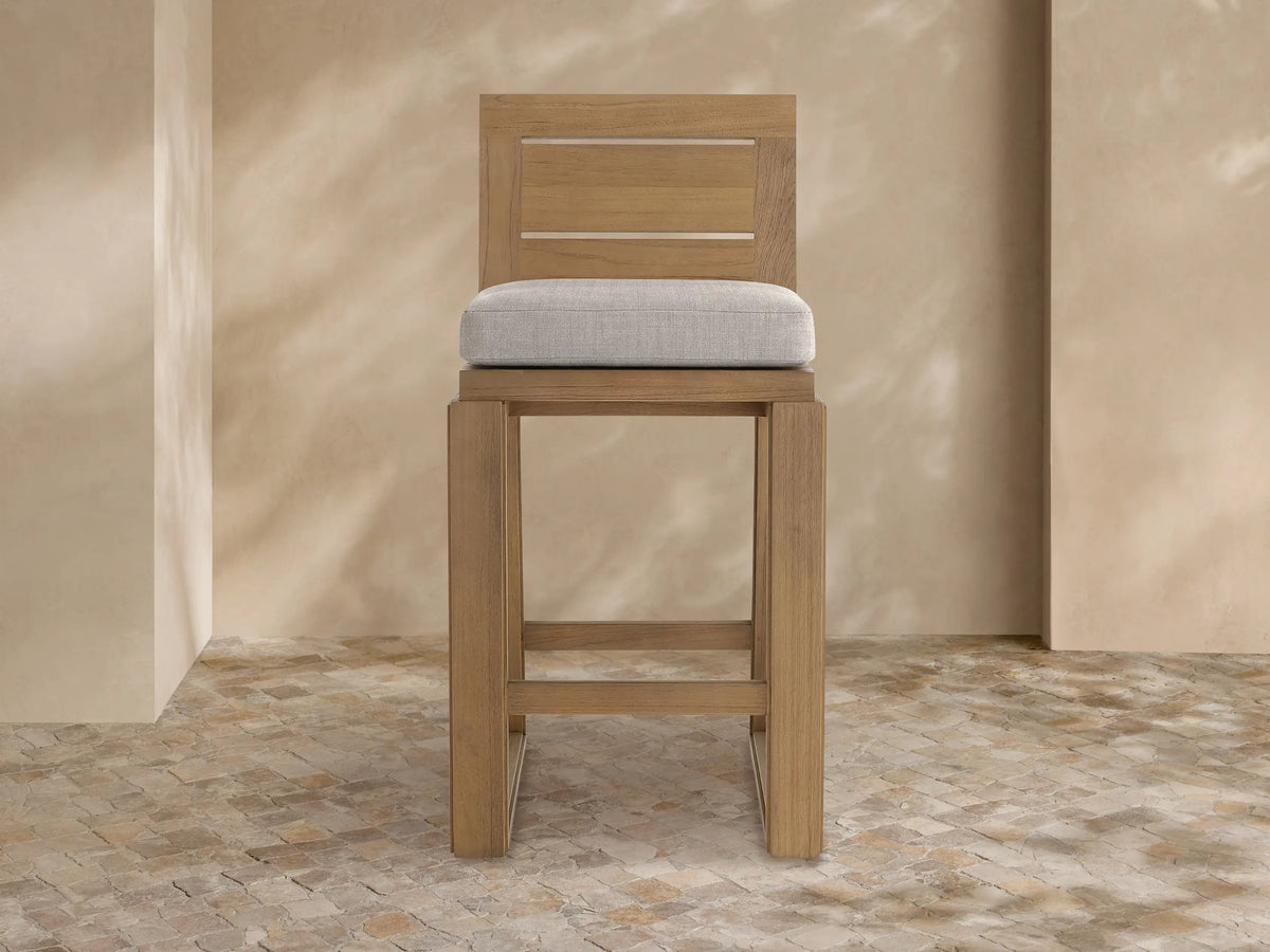 Front view of Canyon Outdoor Teak Barstool. Light brown teak frame, sturdy rectangular legs, slatted backrest, and light grey cushion.