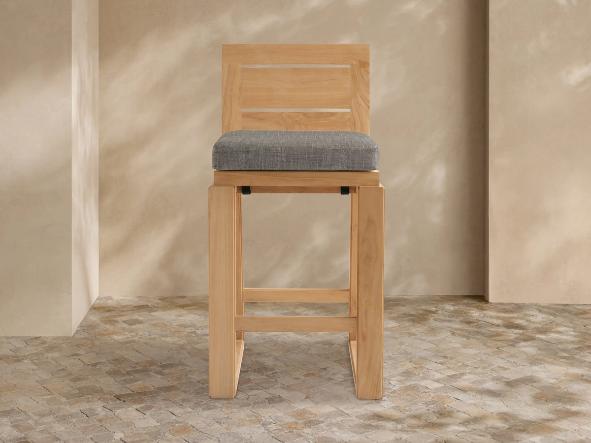 Front view of Canyon Outdoor Teak Barstool. Light brown teak wood frame with two horizontal back slats and a square gray cushion.