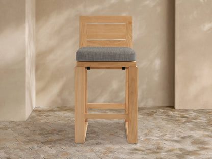 Front view of Canyon Outdoor Teak Barstool. Light brown teak wood frame with two horizontal back slats and a square gray cushion.