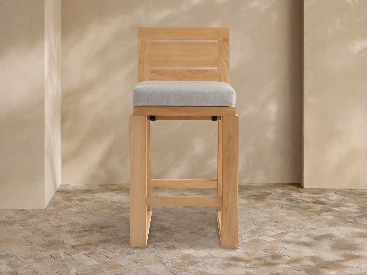 Front view of Canyon Outdoor Teak Barstool with light brown teak wood frame, slatted back, and light gray cushion on white background.