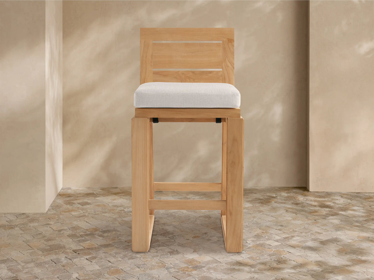 Front view of Canyon Outdoor Teak Barstool, natural teak wood with slatted back, square frame, and light grey cushion.