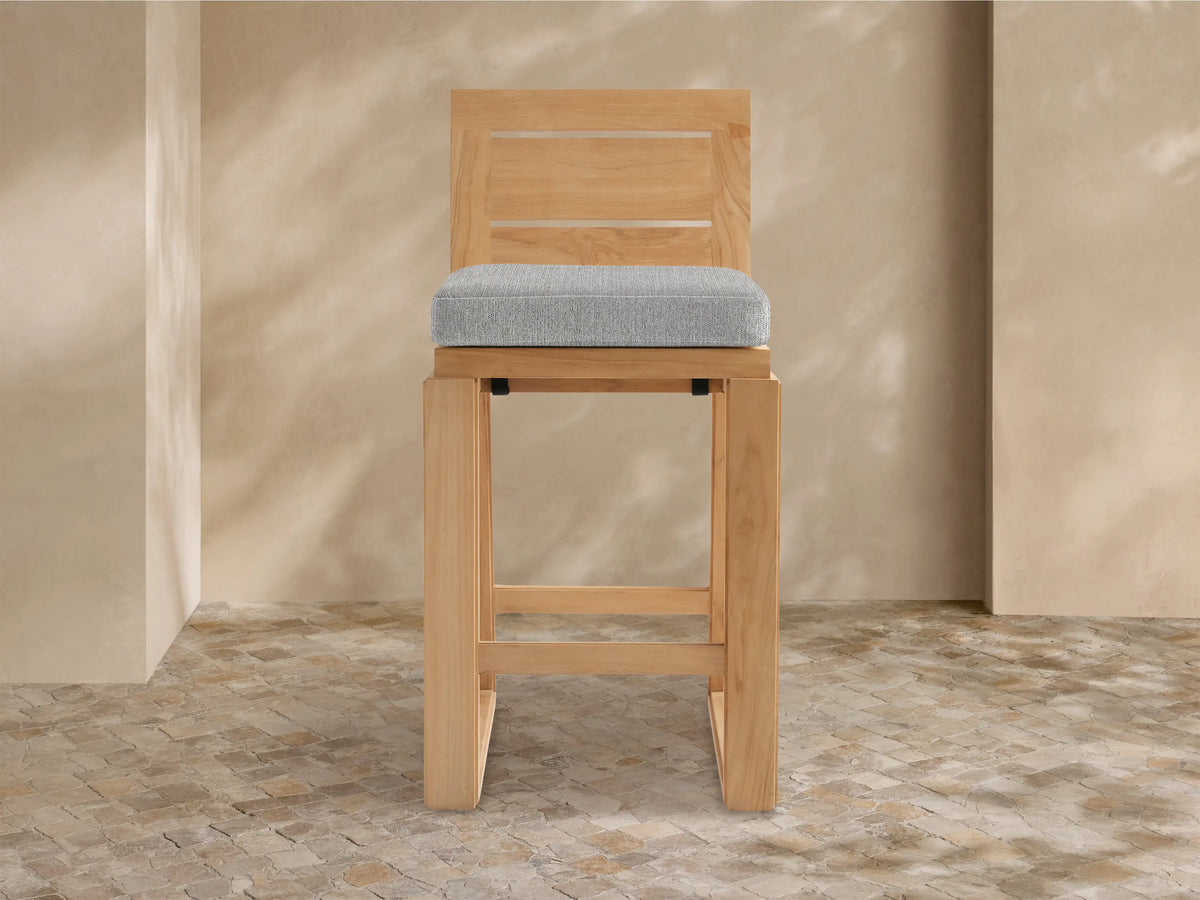 Front view of Canyon Outdoor Teak Barstool. Natural wood frame, slatted back, and light grey seat cushion on white.