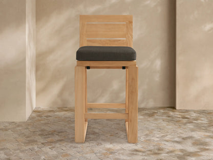 Front view of a Canyon Outdoor Teak Barstool with a natural teak wood frame and a thick dark gray seat cushion.
