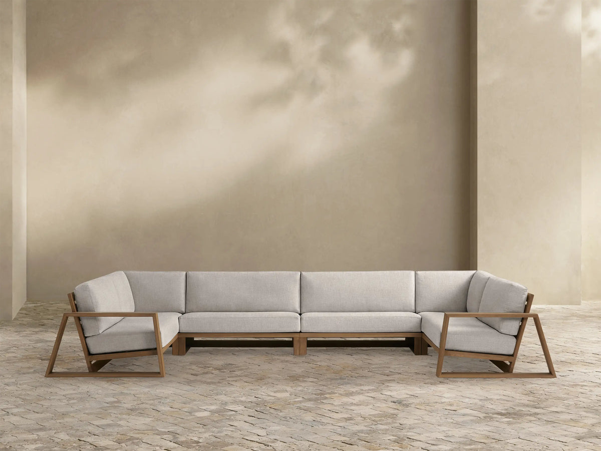 Canyon Outdoor Teak Four-Piece Sectional, U-shaped. Rich brown teak wood frame with open, geometric armrests, light beige cushions.