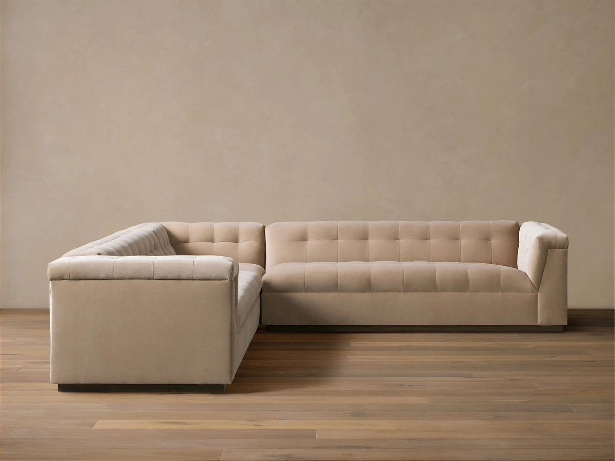 L-shaped Cameran Three-Piece Sectional sofa in light beige, with square-tufted backrests, on a wooden floor against a beige wall.