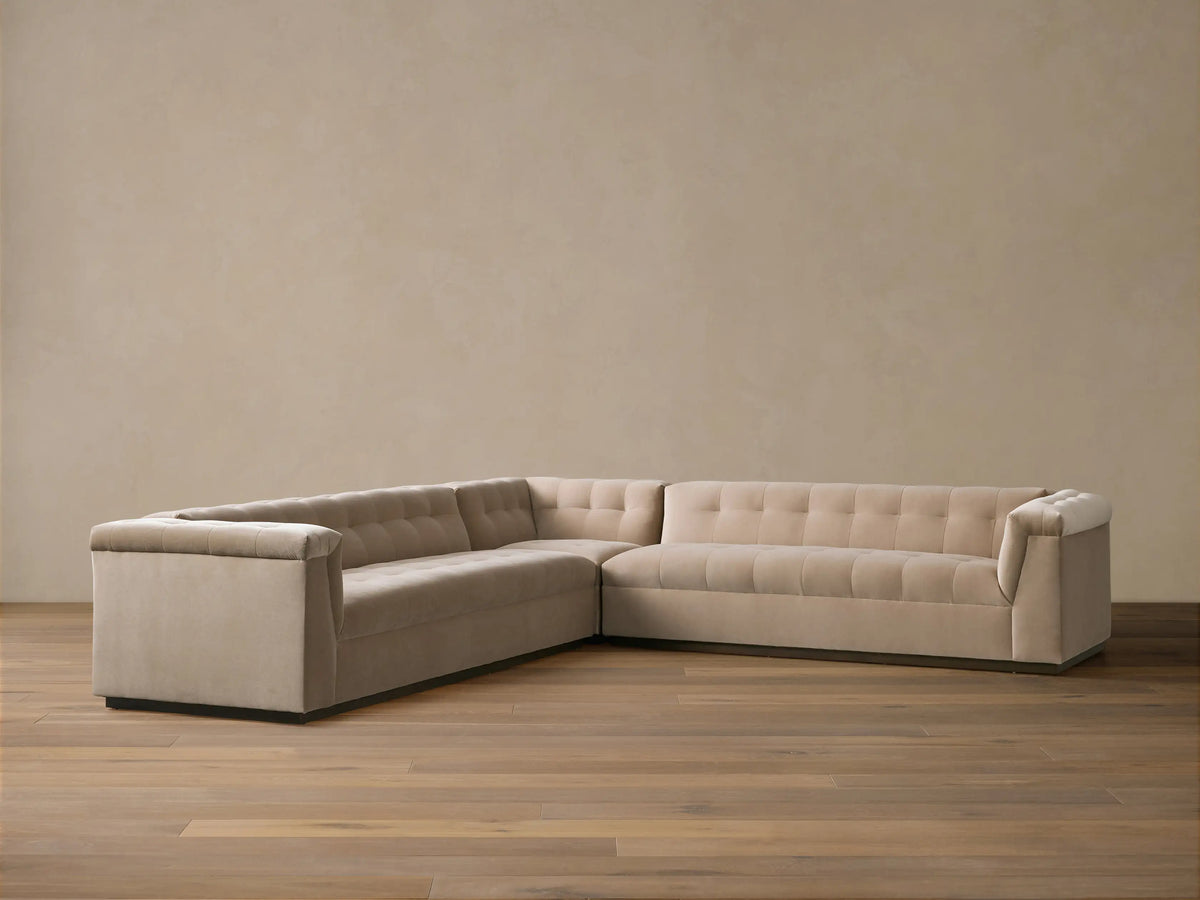 L-shaped Cameran Three-Piece Sectional sofa in light beige, with square-tufted backrests, on a wooden floor against a beige wall.