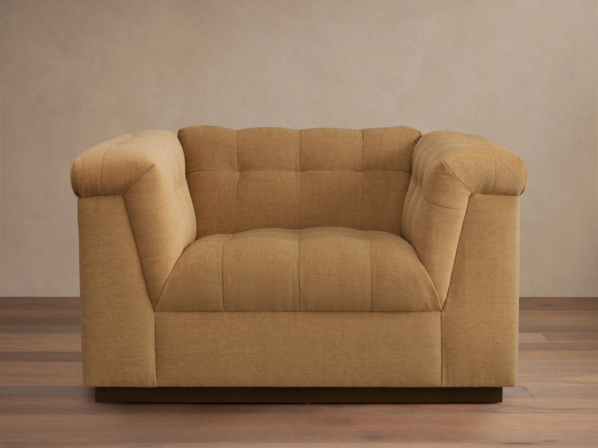 Cameran Chair in light brown fabric, featuring tufted backrests and cushioned armrests, set on a wooden floor against a beige wall.