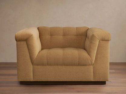 Cameran Chair in light brown fabric, featuring tufted backrests and cushioned armrests, set on a wooden floor against a beige wall.