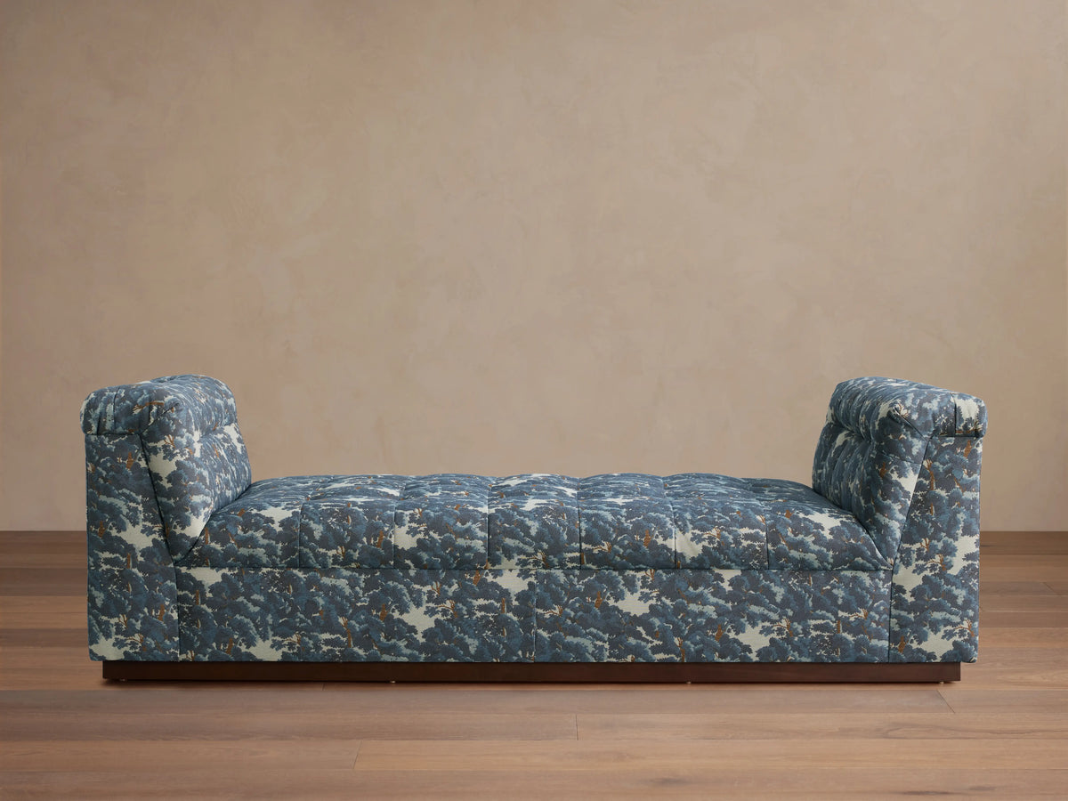 Daybed with patterned upholstery in blue and gray tones, featuring cushioned backrests on each end and set against a neutral wall.