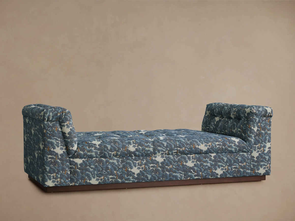 Daybed with patterned upholstery in blue and gray tones, featuring cushioned backrests on each end and set against a neutral wall.