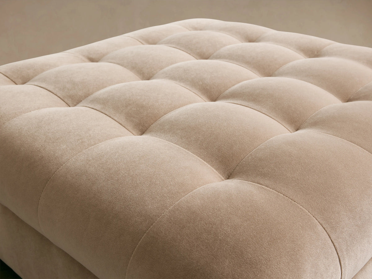Beige Cameran Ottoman with a tufted design and plush, upholstered surface, featuring square stitching and a soft texture.