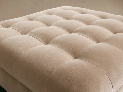 Cameran Ottoman in light beige fabric with tufted square pattern on top, placed on a wooden floor against a neutral wall.