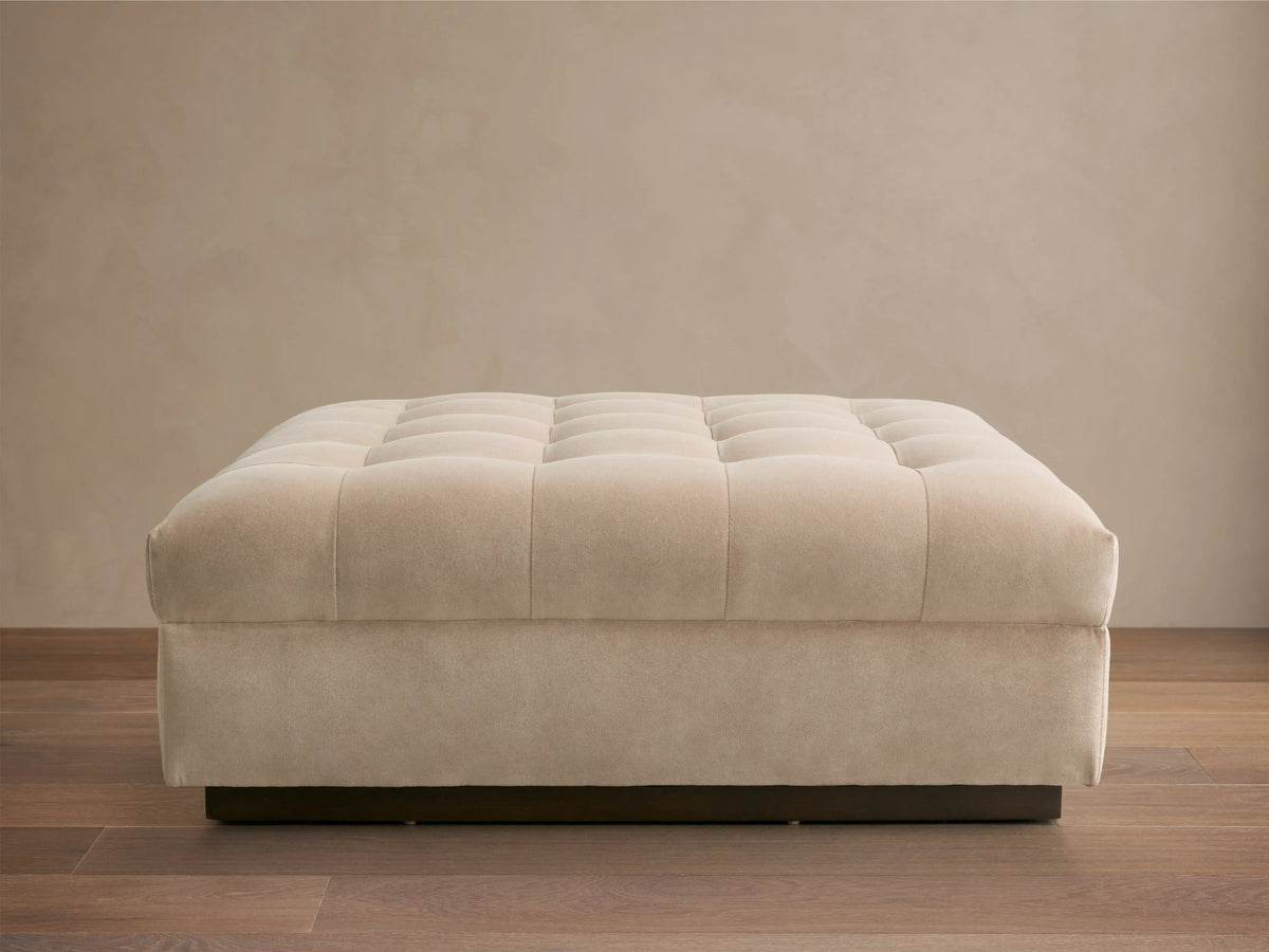 Cameran Ottoman in a soft beige fabric with tufted squares. Close-up shows smooth texture and cushioned appearance.
