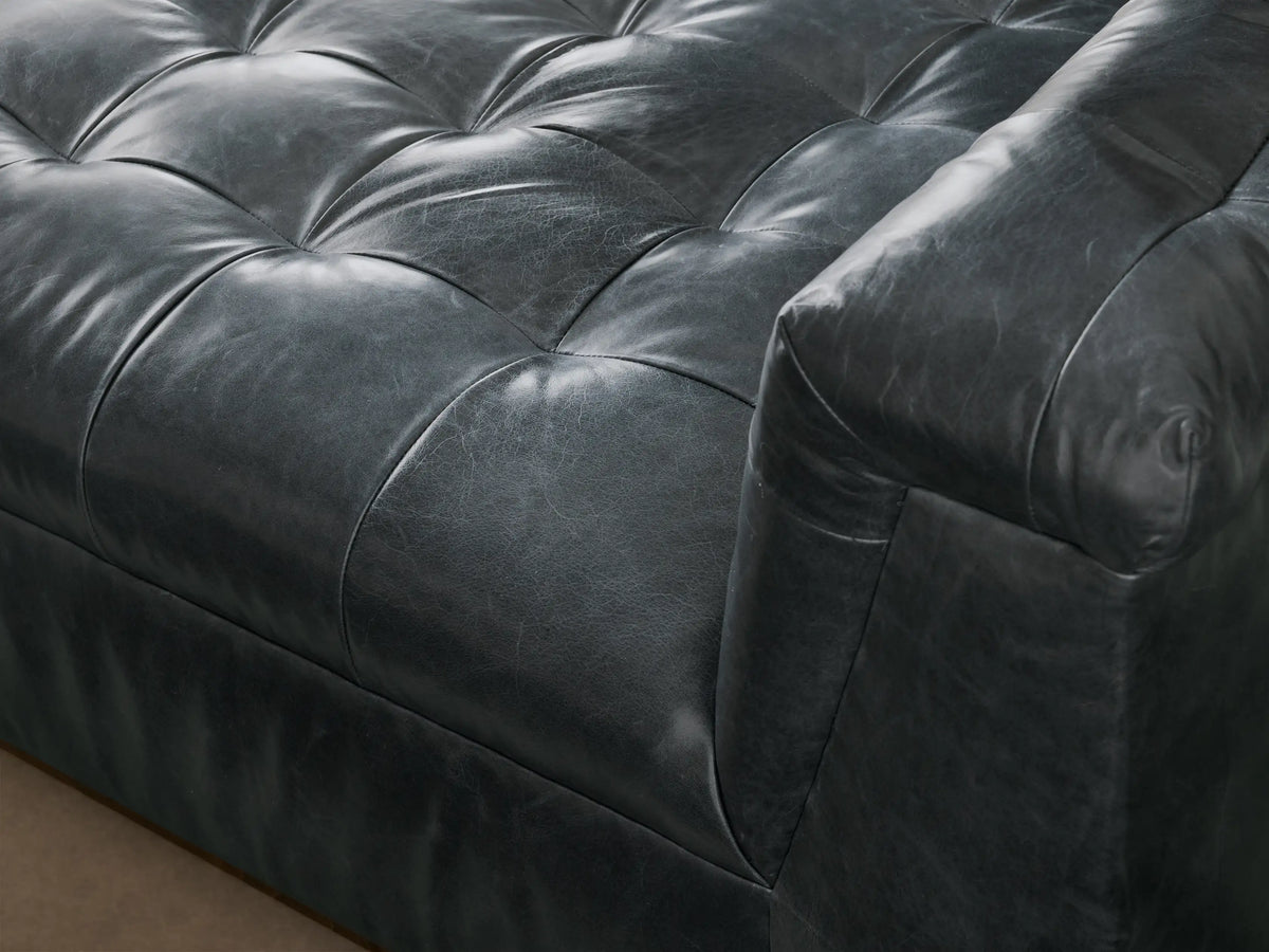 Front and side view of a dark grey Cameran Leather Daybed with tufted seat and armrests, on a wooden base.