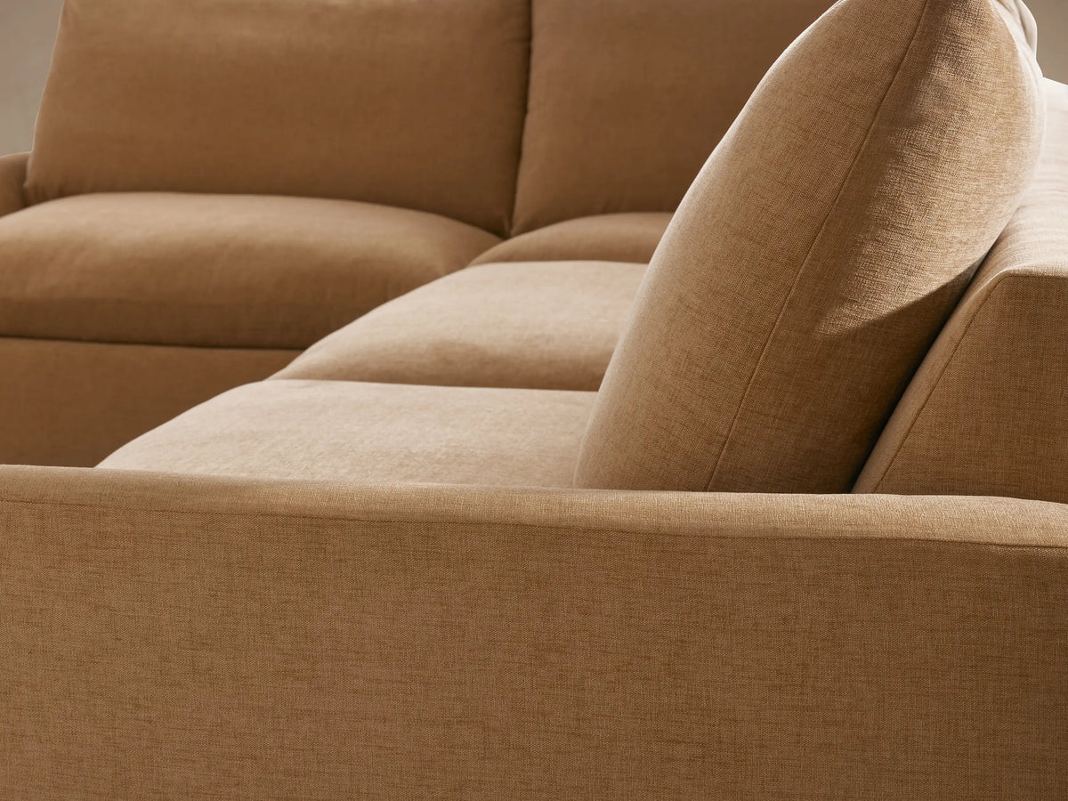 Calistoga two-piece sectional in soft tan fabric, L-shaped design with three cushioned seats and a chaise on the left, set on wooden floor.