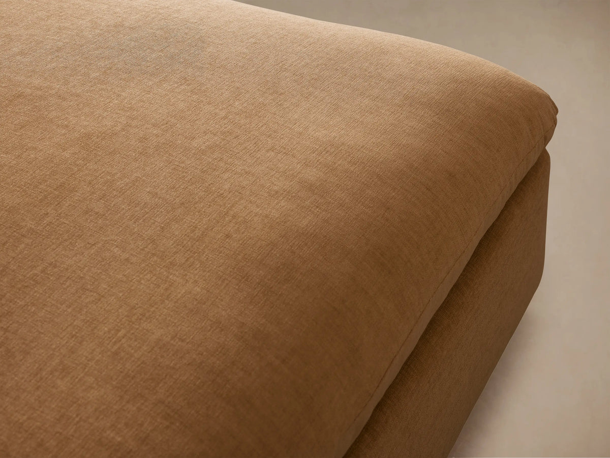 Calistoga Ottoman in beige fabric with a plush cushion top, displayed on a wooden floor against a neutral wall.