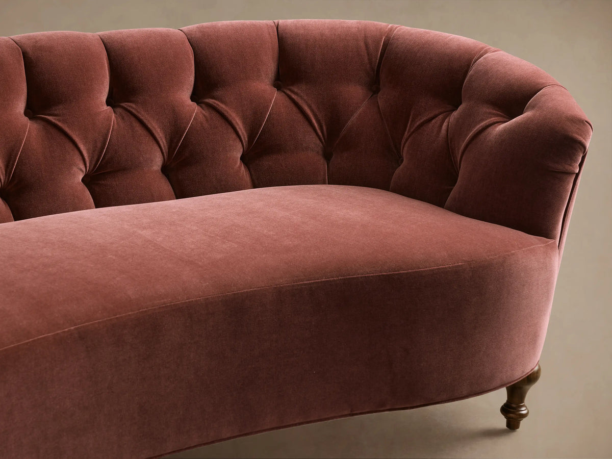 Front view of a dusty rose velvet Cortland Sofa with a curved shape, tufted back, and turned dark wood legs.