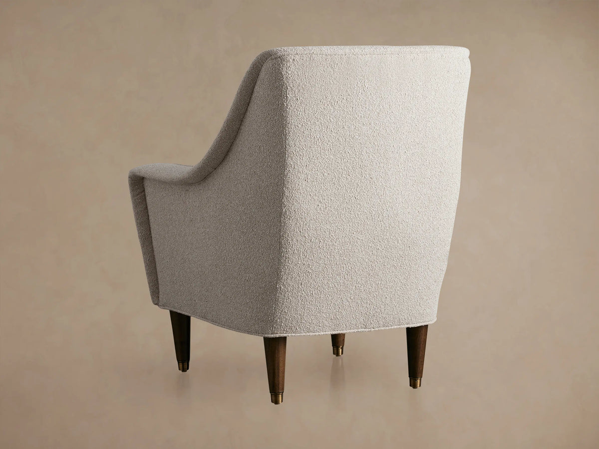 Archie Chair: Angled view of an ecru, textured fabric armchair with curved arms, a seat cushion & dark wooden legs.