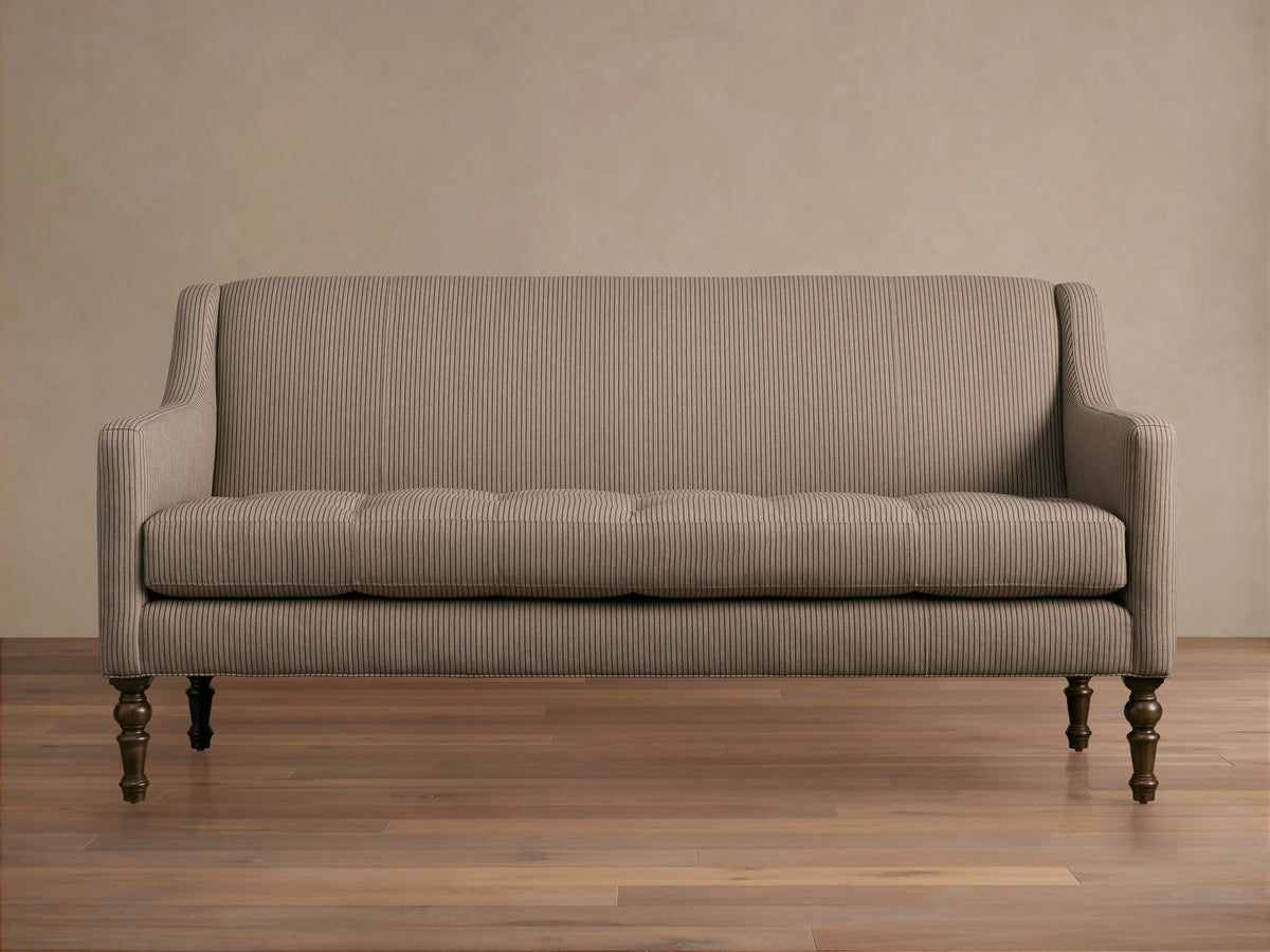 Fenwick Settee: Light beige settee with thin dark vertical stripes, tufted seat, sloped arms, dark turned wood legs, and nailhead trim.