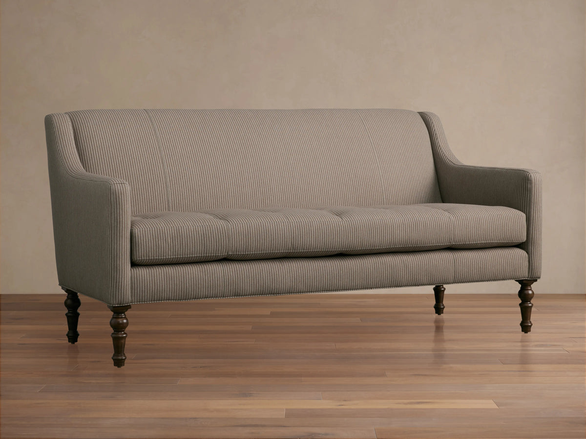 Fenwick Settee: Light beige settee with thin dark vertical stripes, tufted seat, sloped arms, dark turned wood legs, and nailhead trim.