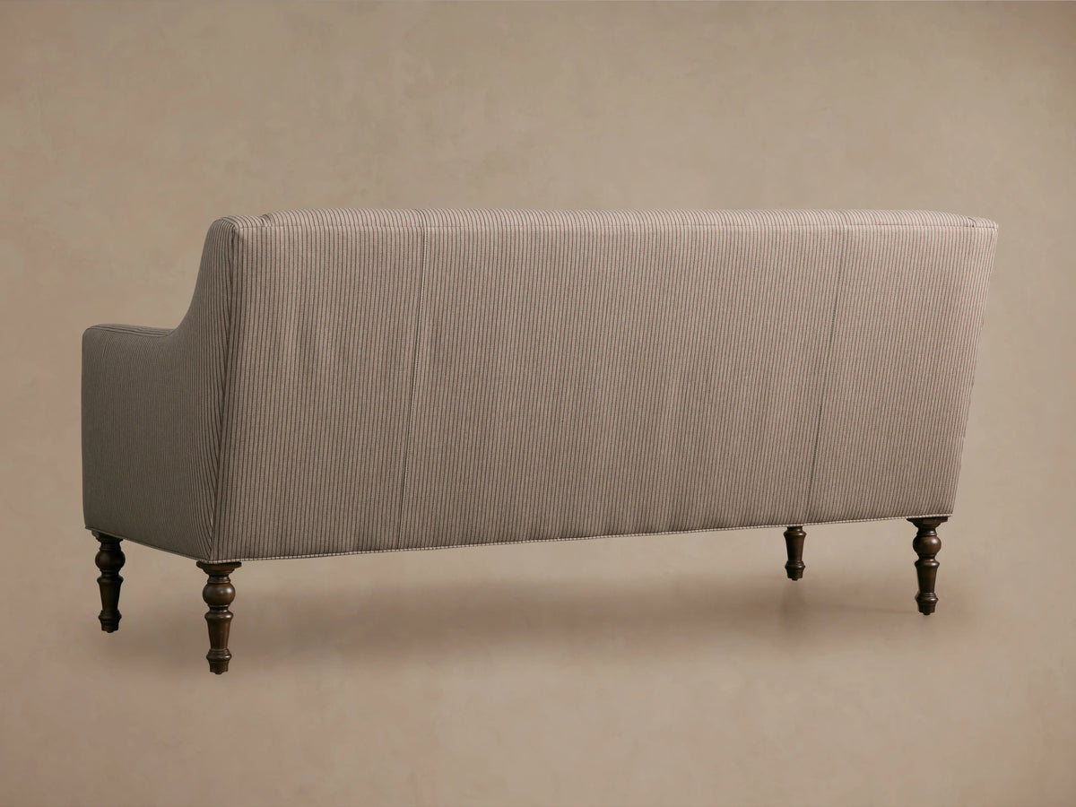 Taupe Fenwick Settee with subtle vertical pinstripes, elegant rolled arms, and dark turned wooden legs on a wood floor.