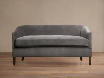 Giles Settee: Dark grey velvety loveseat with curved arms, single seat cushion, and dark wooden legs on a wood floor.