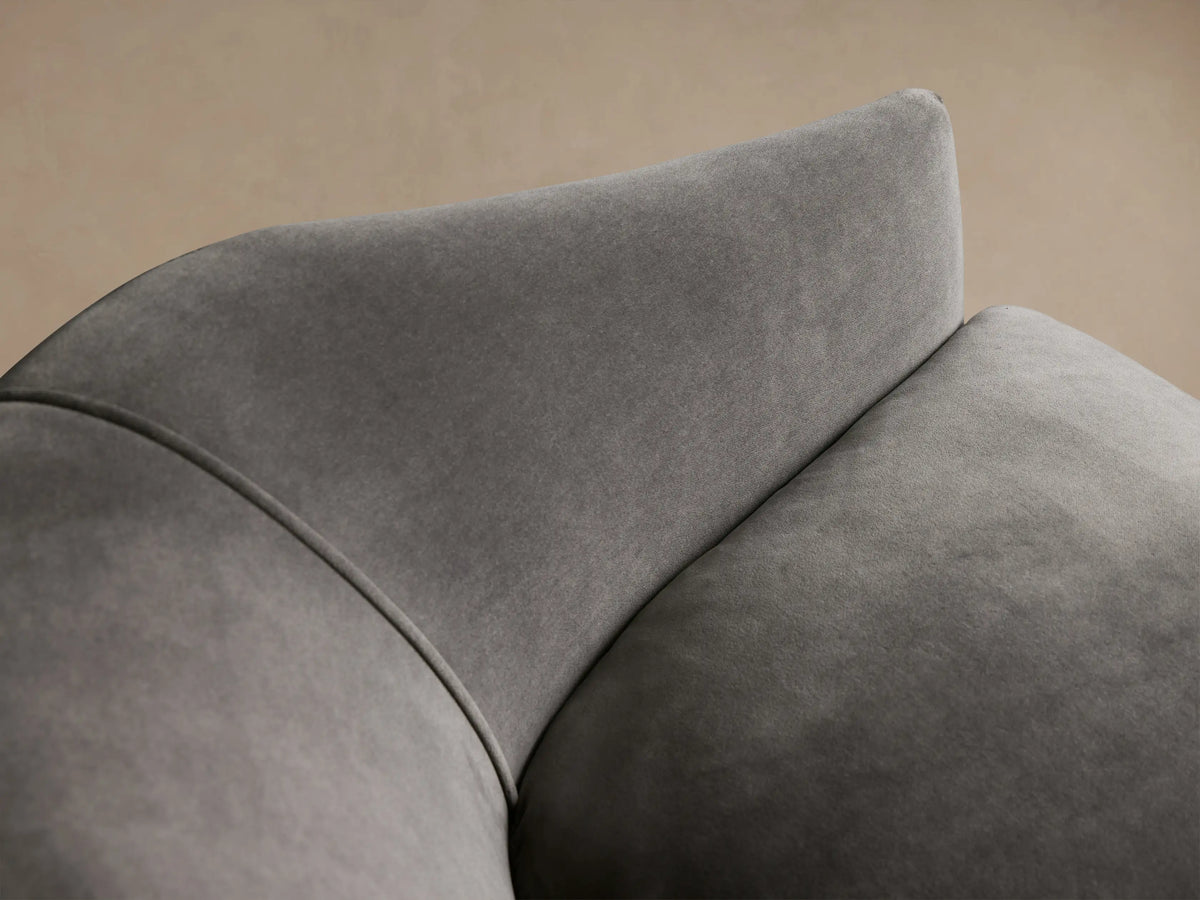 Elegant dark grey velvet Giles Settee, angled left, featuring gracefully curved arms, a single plush cushion, and dark wood legs.